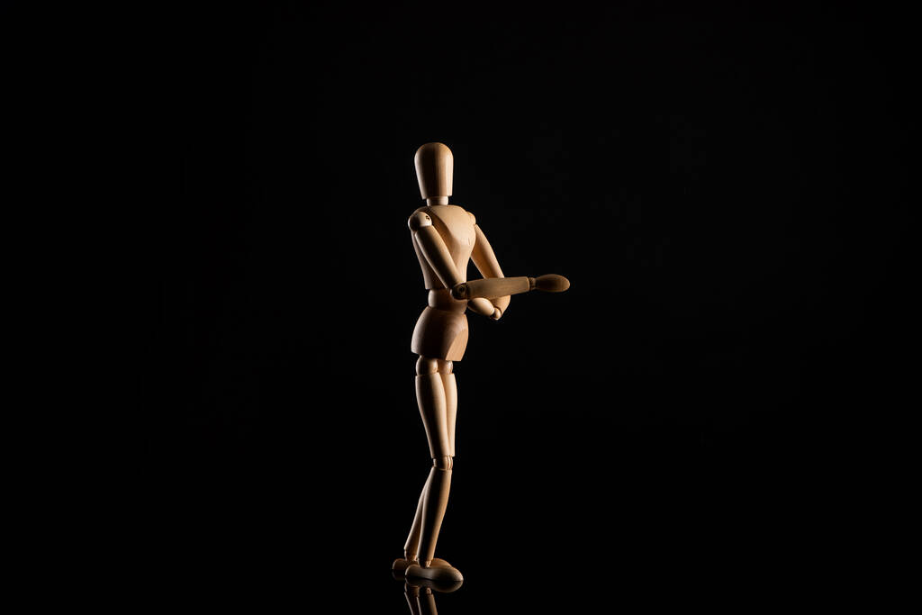 Дерев'яна лялька в стоячому положенні з простягнутою рукою на чорному тлі
 - Фото, зображення