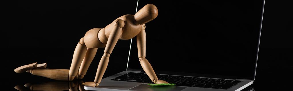 Bambola in legno su tutte e quattro le posizioni imitando spolverare laptop su sfondo nero, colpo panoramico
 - Foto, immagini