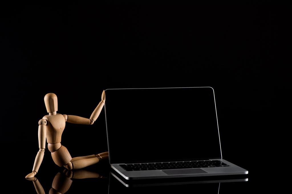 Drewniana lalka w pozycji siedzącej w pobliżu laptopa na czarno  - Zdjęcie, obraz