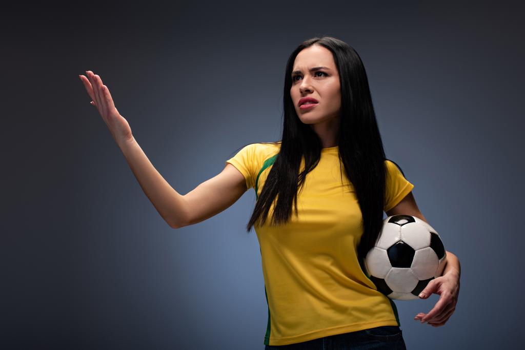 mooie boze voetbal fan holding bal op grijs - Foto, afbeelding