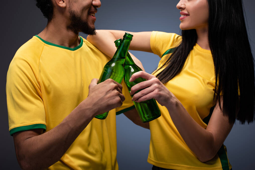 vue recadrée de couples multiethniques de fans de football en t-shirts jaunes cliquetant avec des bouteilles de bière sur gris
 - Photo, image