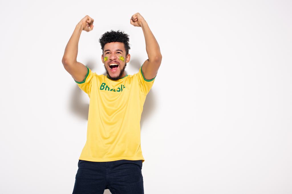 innoissaan afrikkalainen amerikkalainen jalkapallofani keltaisessa t-paidassa, jossa brasilialainen merkki elehtii ja huutaa harmaalla
 - Valokuva, kuva