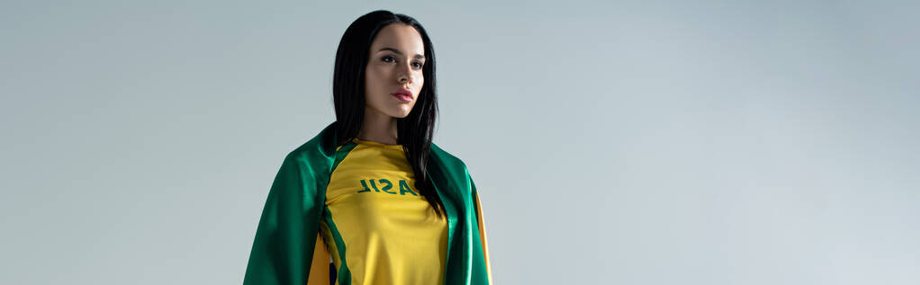 πανοραμική λήψη της ελκυστική γυναίκα οπαδός του ποδοσφαίρου τυλιγμένο σε βραζιλιάνικη σημαία που απομονώνονται σε γκρι - Φωτογραφία, εικόνα