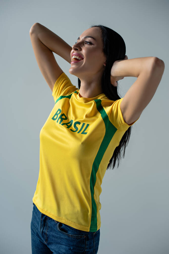 vidám női labdarúgó rajongó sárga pólóban brazil felirattal elszigetelt szürke  - Fotó, kép