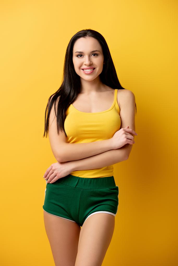 vonzó mosolygós lány zöld rövidnadrágban áll keresztbe tett karokkal sárga   - Fotó, kép