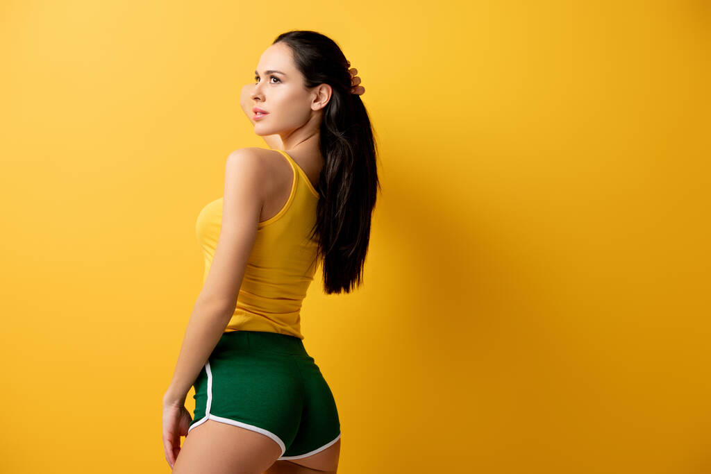 aantrekkelijk meisje staan in groen shorts op geel  - Foto, afbeelding