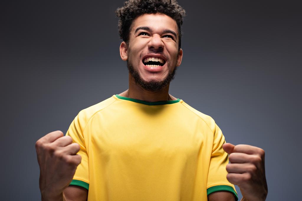 Sarı tişörtlü Afro-Amerikan futbol fanatiği bağırıyor ve gri renkli jestler yapıyor. - Fotoğraf, Görsel