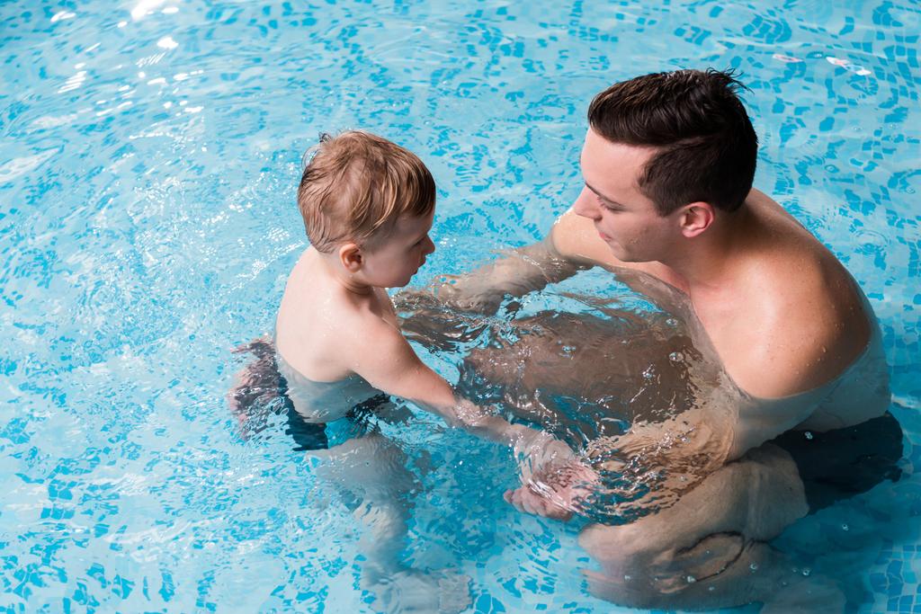 Blick von oben auf glückliche Schwimmtrainerin, die Kleinkind im Schwimmbad unterrichtet  - Foto, Bild