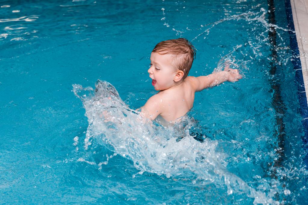 Aufgeregter Kleinkind-Junge planscht Wasser in Schwimmbad  - Foto, Bild