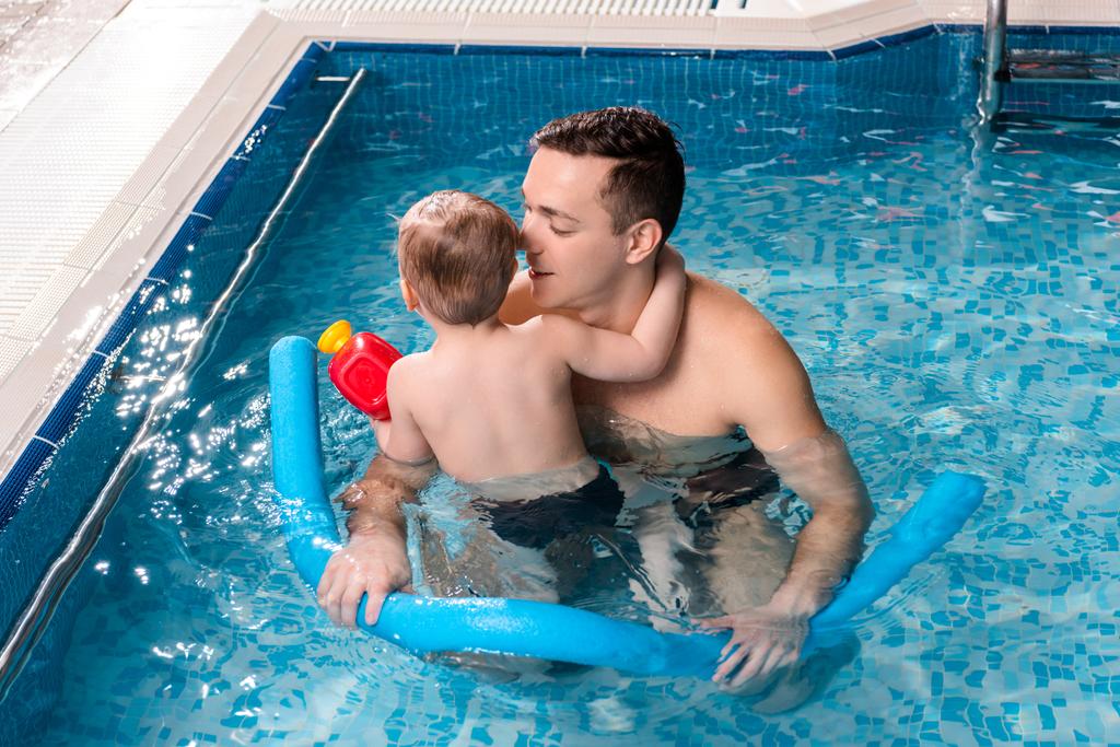 handsome swim trainer swimming with toddler kid and holding pool noodle  - Photo, Image