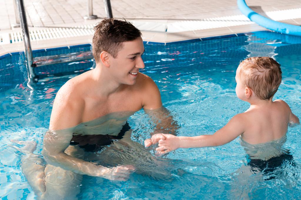 pozitív úszás tréner kéz a kézben kisfiúval a medencében  - Fotó, kép
