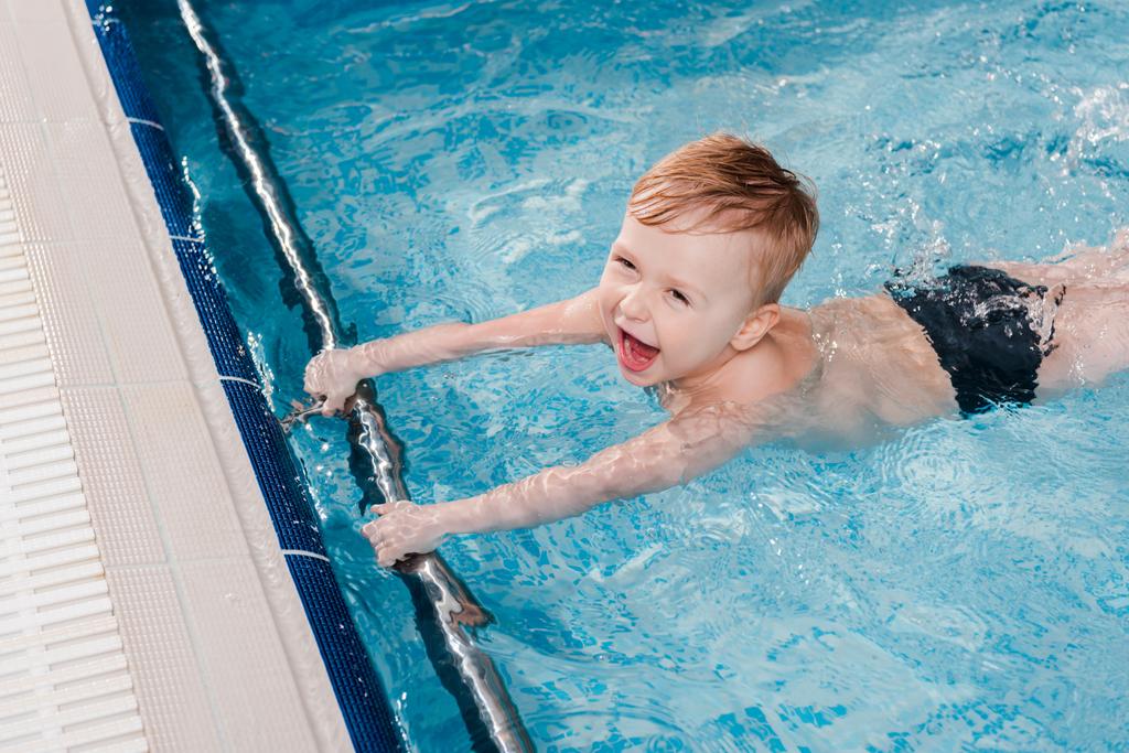vista aérea del niño emocionado nadando cerca de las tablas de aleteo en la piscina
  - Foto, Imagen