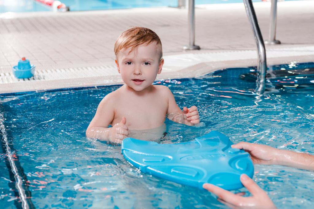 Тренер по плаванию держит пульт управления рядом с симпатичным мальчиком-малышом в бассейне
  - Фото, изображение