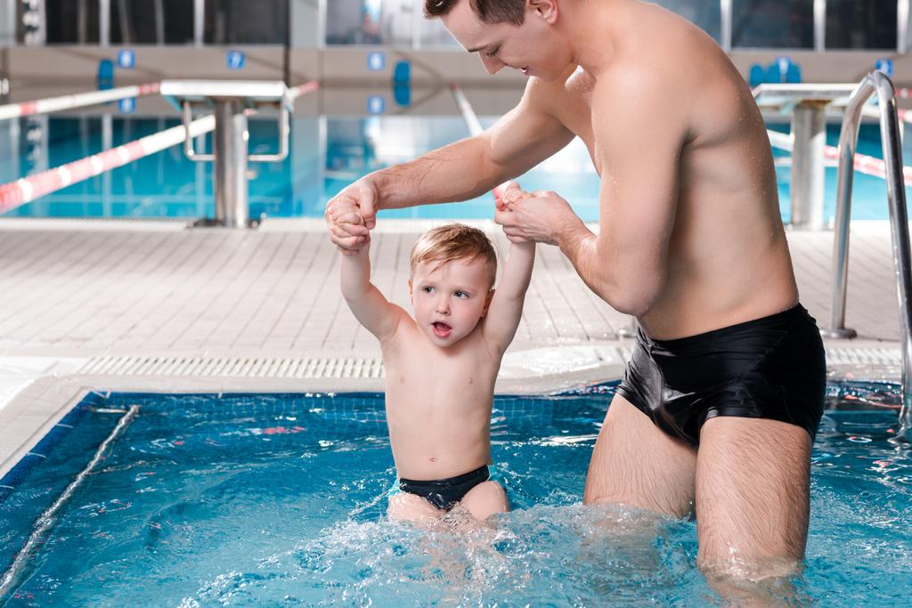水泳コーチは水泳プールで幼児と手を携えて  - 写真・画像