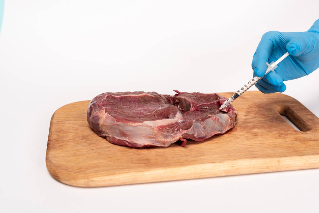 Άποψη του γιατρού με σύριγγα που κάνει ορμονική ένεση σε ωμό κρέας σε ξύλο κοπής που απομονώνεται σε λευκό - Φωτογραφία, εικόνα