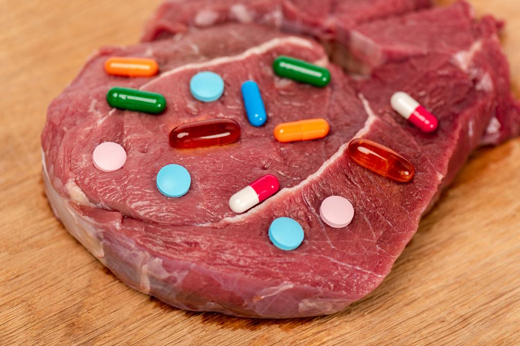 Közelkép a hormonális tabletták egy darab nyers hús fa felületen - Fotó, kép