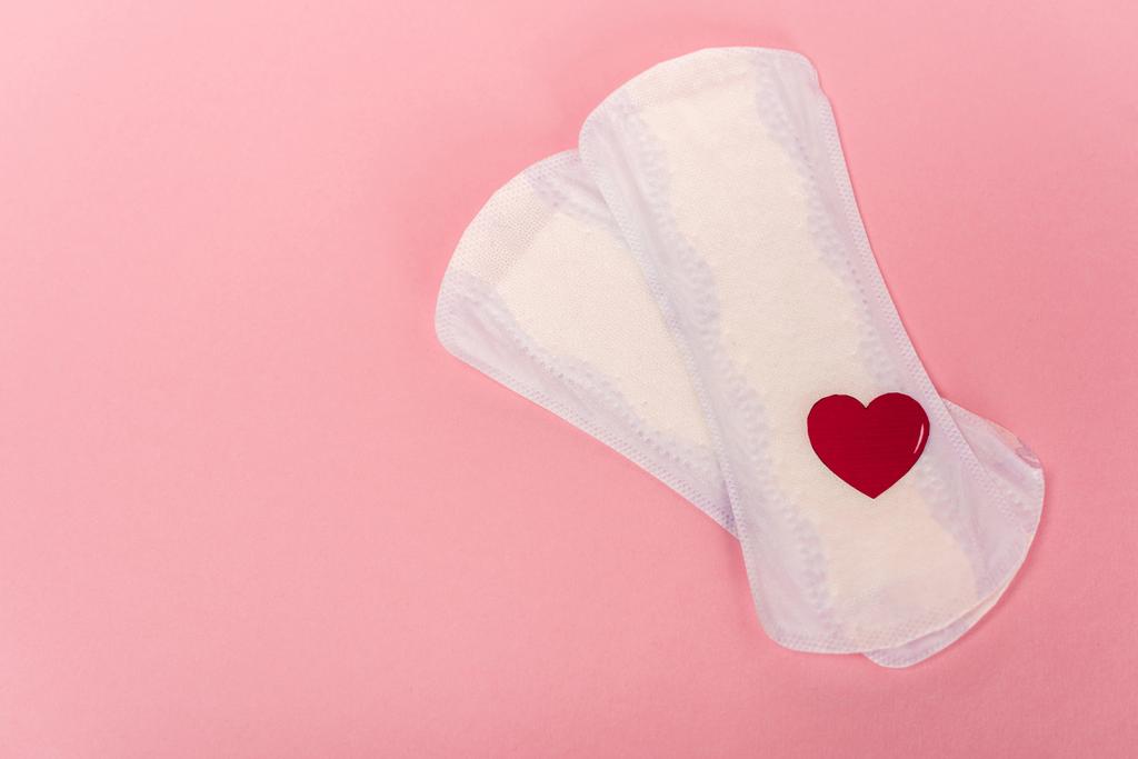 Horní pohled na ženské podložky s papírovým srdcem na růžovém pozadí - Fotografie, Obrázek