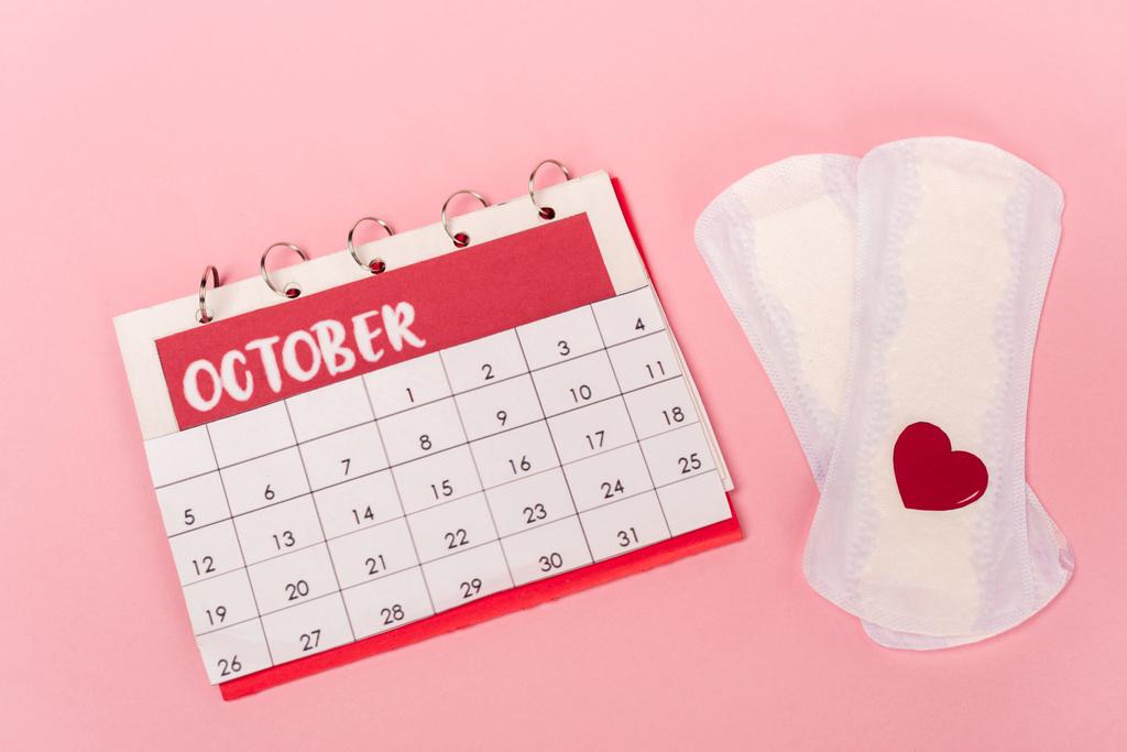 High angle view of feminine pads with paper heart and calendar on pink background - Photo, Image