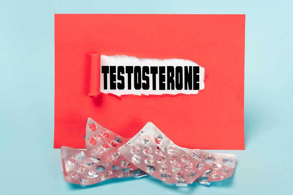 Papier met testosteron belettering en lege blisters van pillen op blauwe achtergrond - Foto, afbeelding