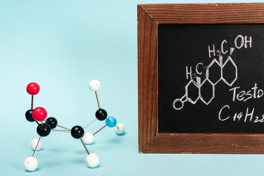 Construção de hormônio perto de quadro-negro com fórmula de testosterona no fundo azul
 - Foto, Imagem