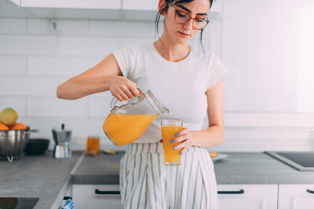 Tyttö kaatamalla appelsiinimehua keittiössä
 - Valokuva, kuva