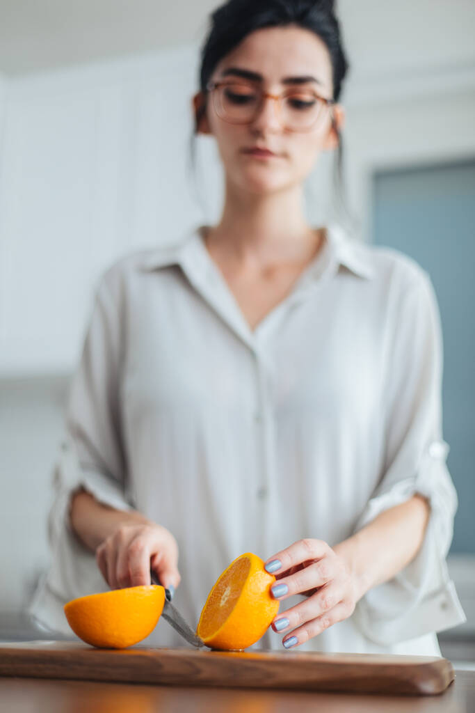 Beautiful young woman cutting orange on the kitchen counter - Photo, Image