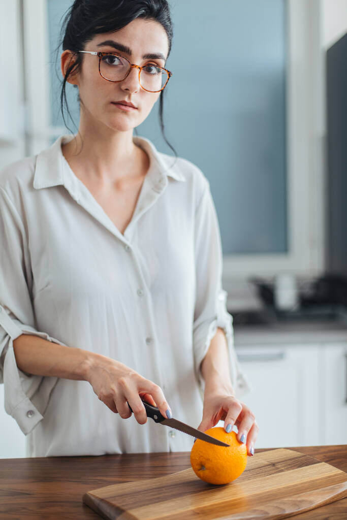 mooie jonge vrouw snijden oranje op de keuken teller - Foto, afbeelding