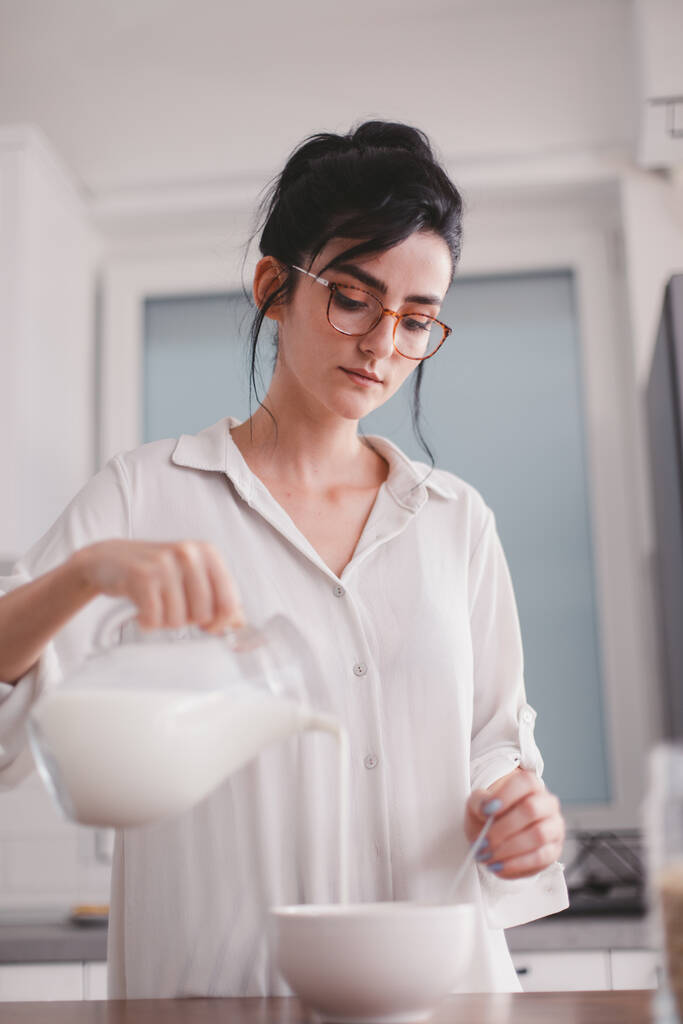 Piękna młoda kobieta wlewa mleko do miski - Zdjęcie, obraz