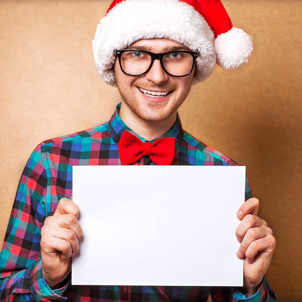 Хипстер в шляпе Санта-Клауса держит лист бумаги
. - Фото, изображение
