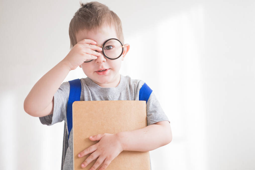 Niño pequeño en gafas con mochila y libro. Preescolar en gafas. Regreso al concepto escolar
  - Foto, imagen