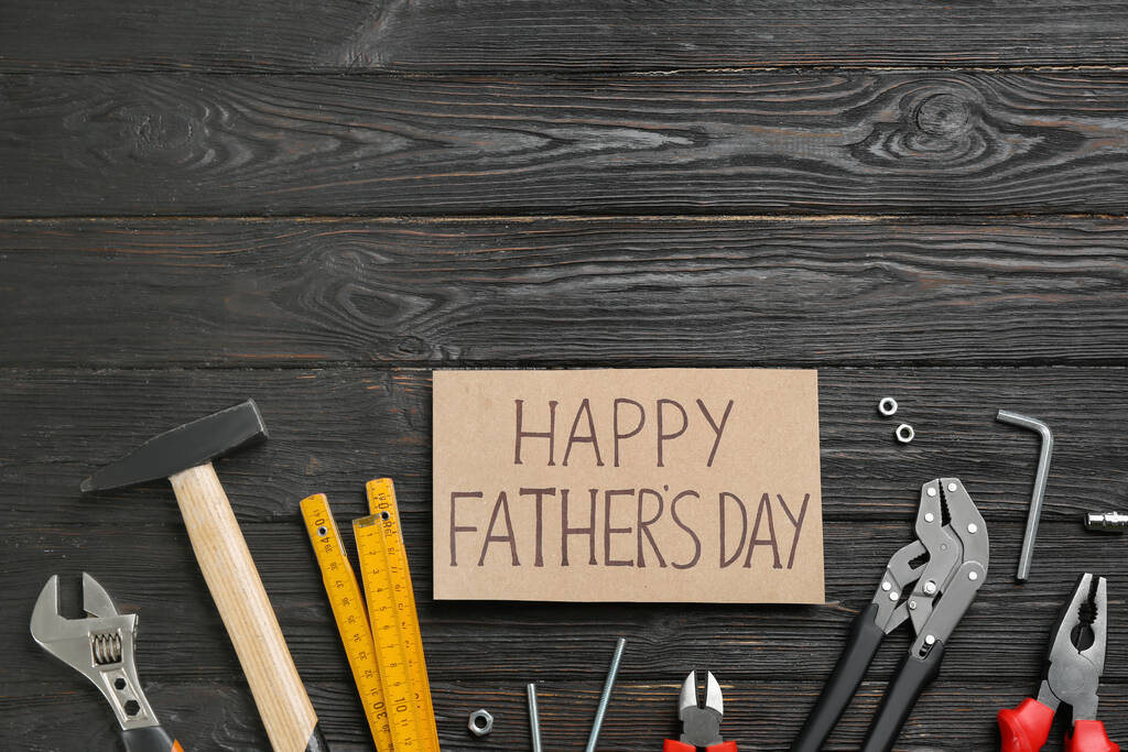 Card with phrase HAPPY FATHER'S DAY and different tools on black wooden background, flat lay. Space for text - Photo, Image