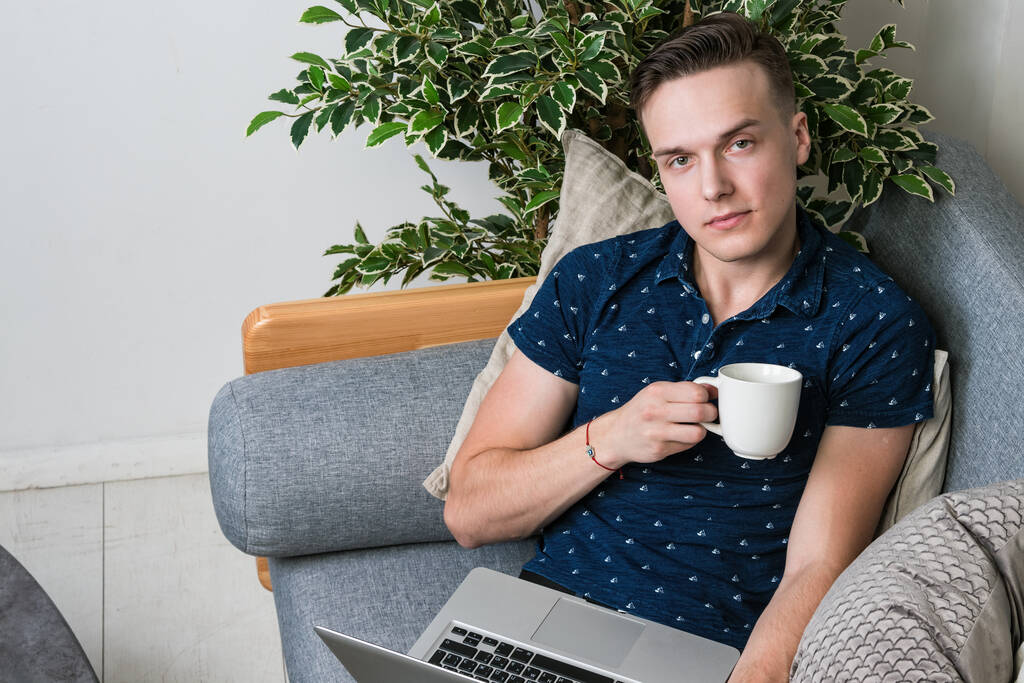 Young happy freelancer working with laptop while sitting on couch - Photo, Image