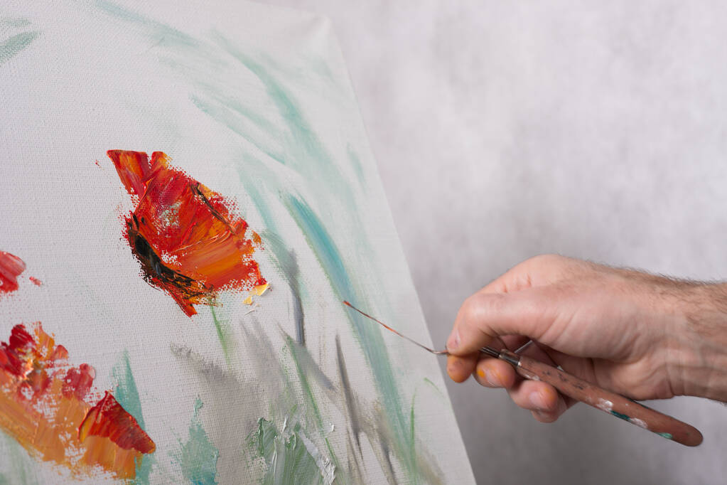 パレットナイフを持ったアーティストが白いキャンバスに赤い花を描きます。絵の始まり - 写真・画像