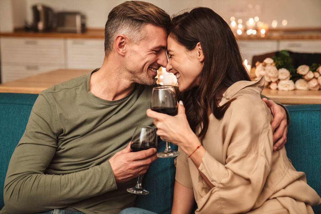 Imagem de casal apaixonado feliz beber vinho tinto de óculos, tendo jantar romântico à luz de velas em casa
 - Foto, Imagem