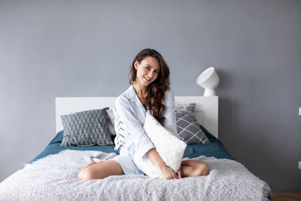 Una mujer encantadora en la cama abraza una almohada. Retrato de una linda chica en el dormitorio
. - Foto, imagen