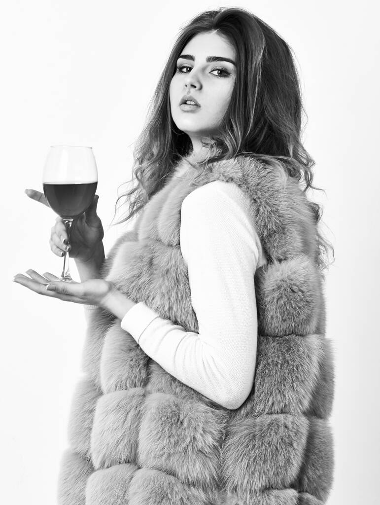 Hedonism concept. Reasons to drink red wine in wintertime. Woman drink wine. Girl fashion makeup wear fur coat hold wine glass. Lady fashion model curly hairstyle likes expensive luxury wine - Photo, Image