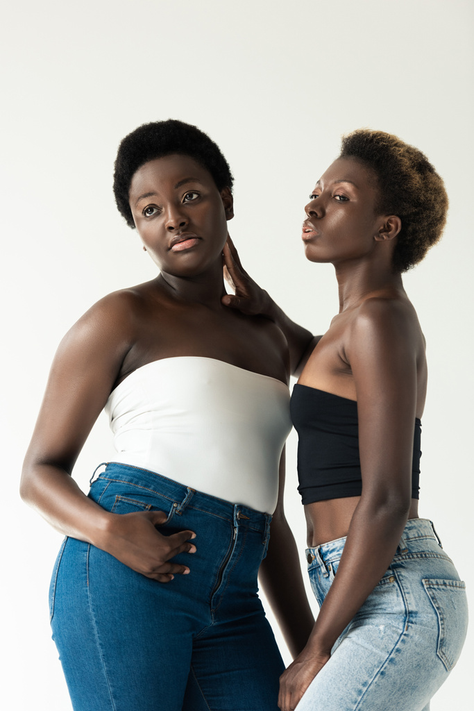 afrikanisch-amerikanische Freundinnen in Jeans und Tops umarmen sich vereinzelt auf grau   - Foto, Bild