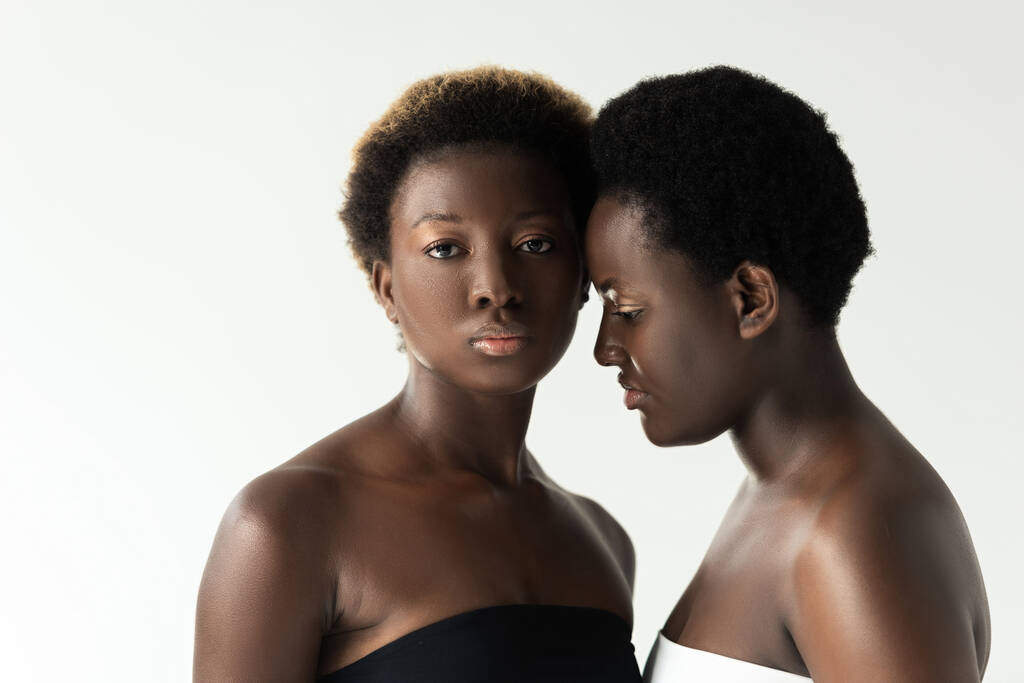 Afroamerikanerinnen in Tops berühren Stirn isoliert auf grau  - Foto, Bild