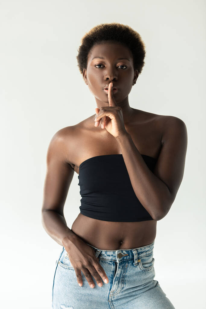 Afrikkalainen amerikkalainen tyttö farkut ja musta toppi osoittaa hiljaisuus symboli eristetty harmaa
 - Valokuva, kuva