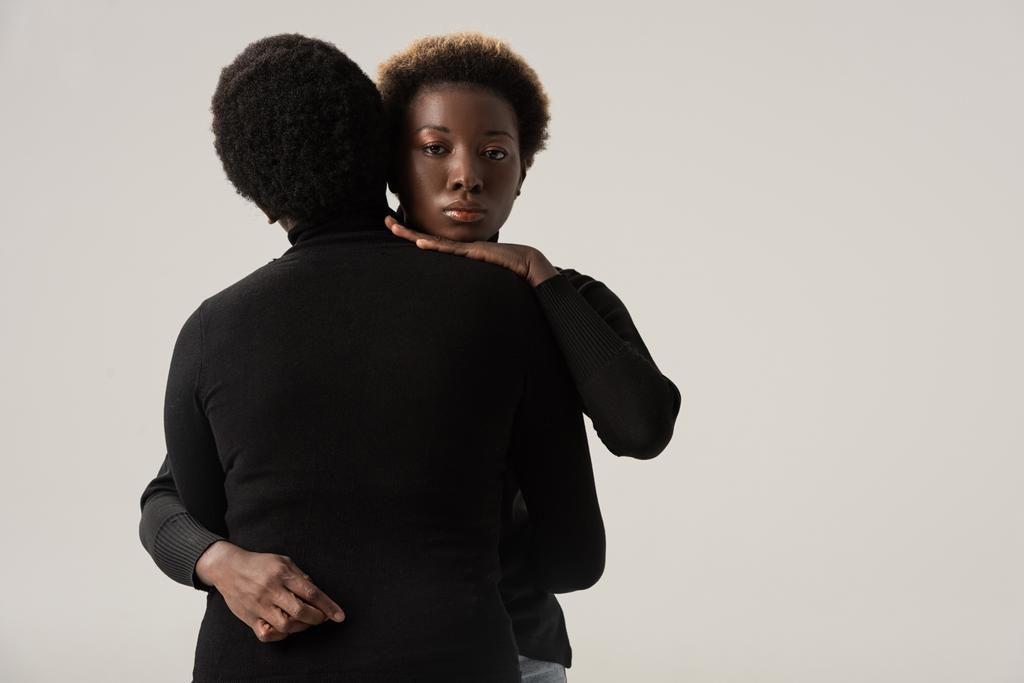 chicas afroamericanas atractivas en cuellos altos negros abrazándose aisladas en gris
 - Foto, imagen