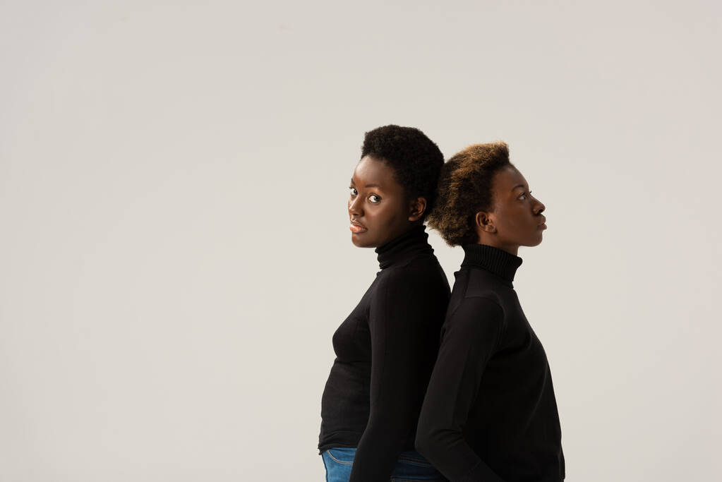 Afrikkalainen amerikkalainen tyttöystäviä musta poolopaidat seisoo selkä selkää vasten eristetty harmaa
 - Valokuva, kuva