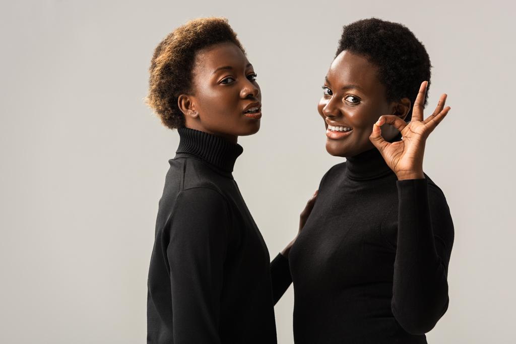 fröhliche afrikanisch-amerikanische Mädchen in schwarzen Rollkragenpullovern zeigen ok Zeichen isoliert auf grau - Foto, Bild