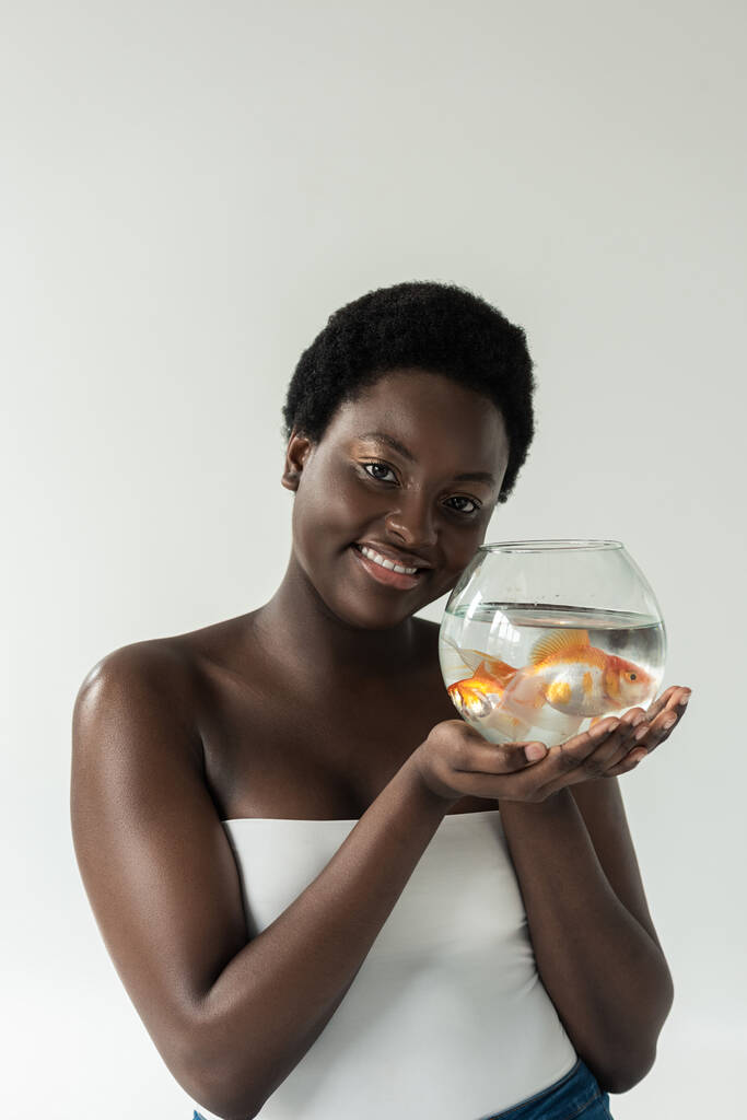 vrolijk Afrikaans amerikaans meisje houden aquarium met vis geïsoleerd op grijs - Foto, afbeelding