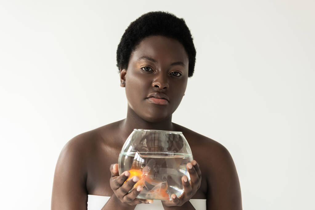 attractive african american girl holding aquarium with fish isolated on grey - Photo, Image