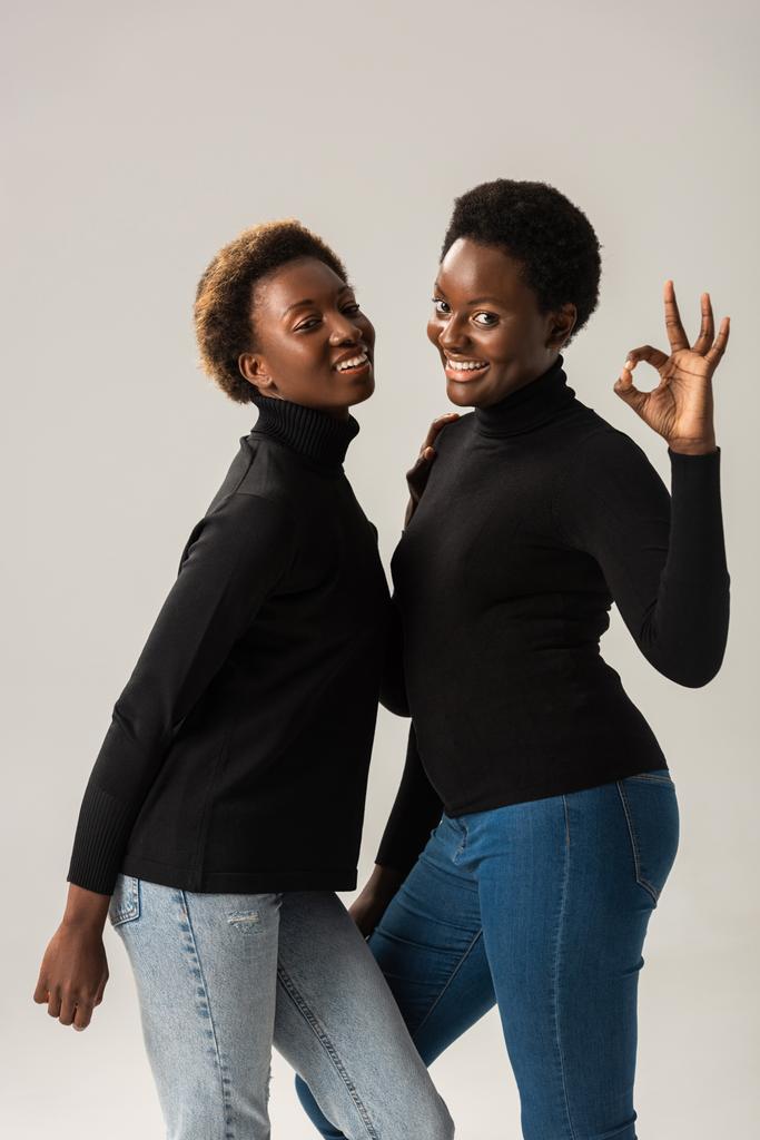 sorrindo meninas americanas africanas em golas pretas mostrando sinal ok isolado em cinza
 - Foto, Imagem