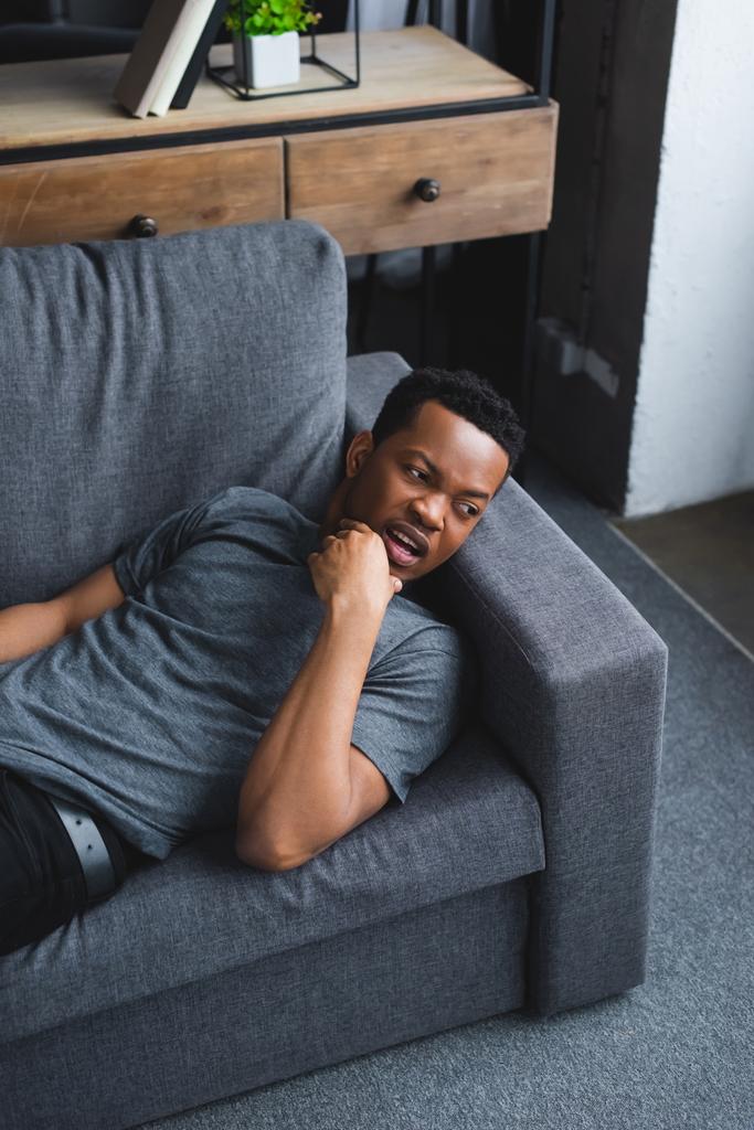 Homme afro-américain inquiet allongé sur le canapé à la maison
 - Photo, image