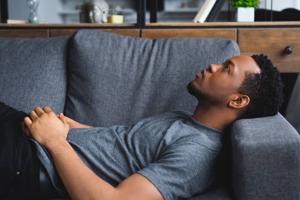 solitario africano americano hombre acostado en sofá en casa
 - Foto, Imagen