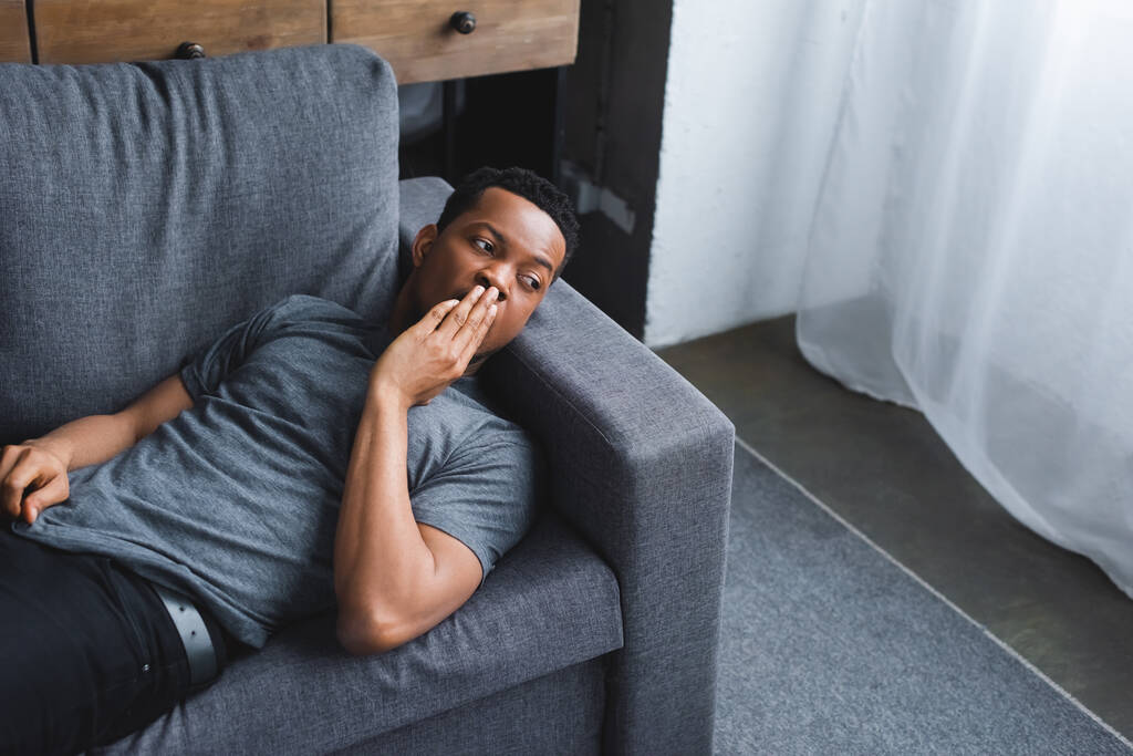 Worried african american man lying on sofa at home - Photo, Image