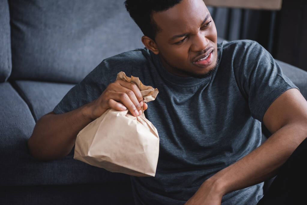 Huolestunut afrikkalainen amerikkalainen mies pitää paperipussia, kun hänellä on paniikkikohtaus kotona
 - Valokuva, kuva