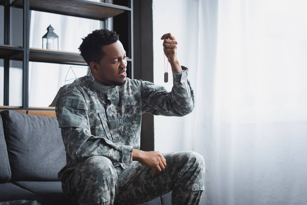 benadrukte Afro-Amerikaanse soldaat kijkt naar leger badge thuis, lijden aan PTSS - Foto, afbeelding